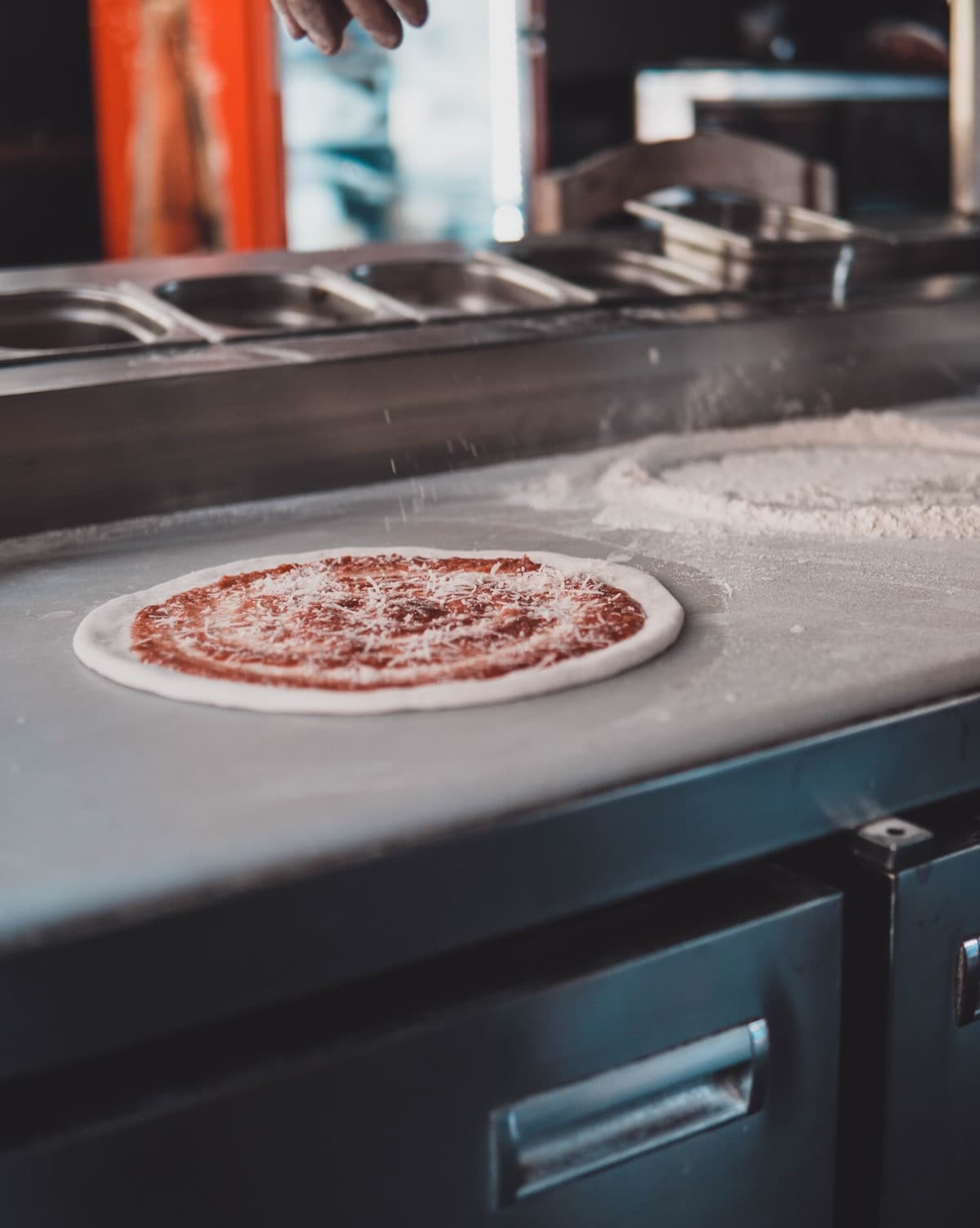 Προετοιμασία πίτσας για ψήσιμο επάνω σε ανωξείδωτο πάγκο κουζίνας