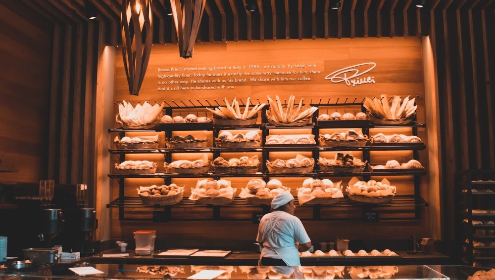 Αρτοποιείο γεμάτο με ψωμιά και υπάλληλο μπροστά