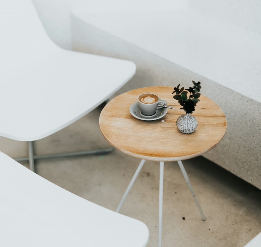 Λευκές καρέκλες και μικρό τραπεζάκι με καφέ επάνω σε μίνιμαλ διακόσμηση καφετέριας