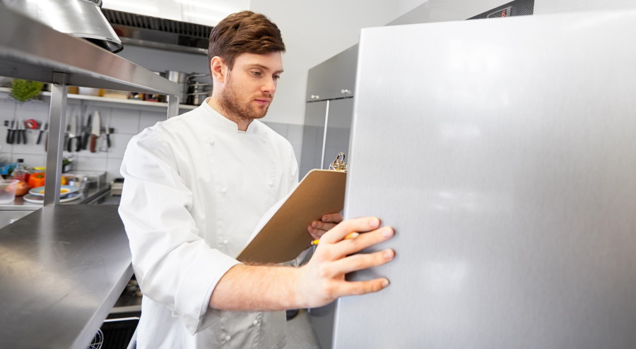Άνδρας με λευκή στολή μπροστά σε επαγγελματικό ψυγείο σε κουζίνα μαζικής εστίασης